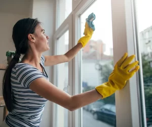 October Home Checklist. A woman with yellow, rubber gloves cleaning her windows.