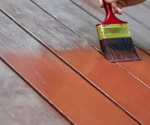 October Home Checklist. Someone refinishing their deck with orange stain and a red paint brush.
