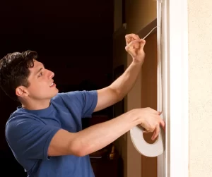 A man in a blue shirt putting gray weather stripping around the doorway.