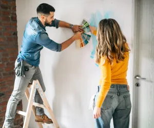 A man holding up a bunch of paint swatches on the wall for the woman to choose from.