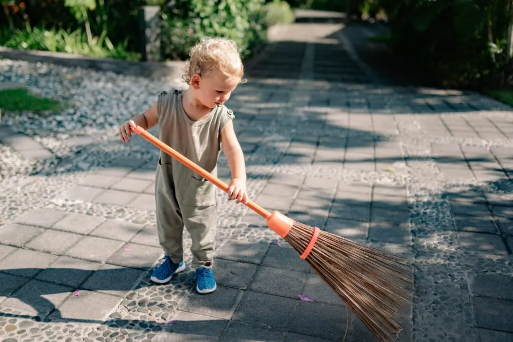 child using toy broom to sweep up sidewalk
