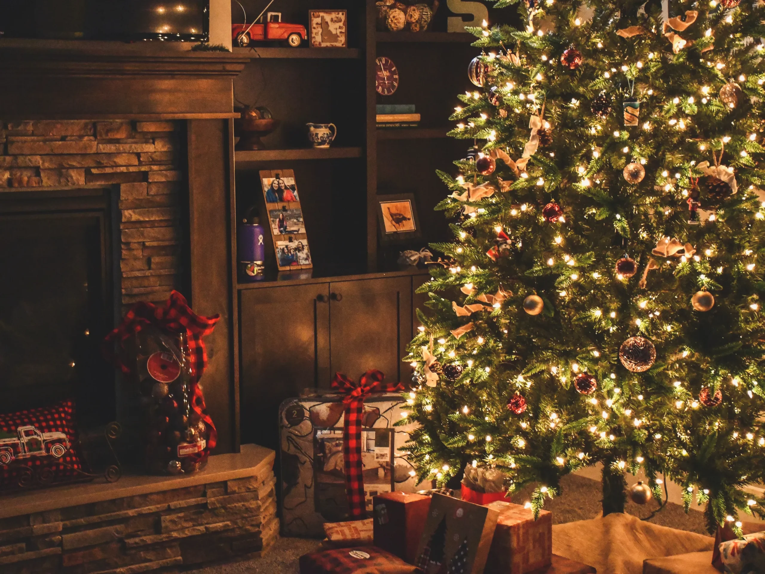 Christmas tree lit up next to a collection of presents by the fireplace